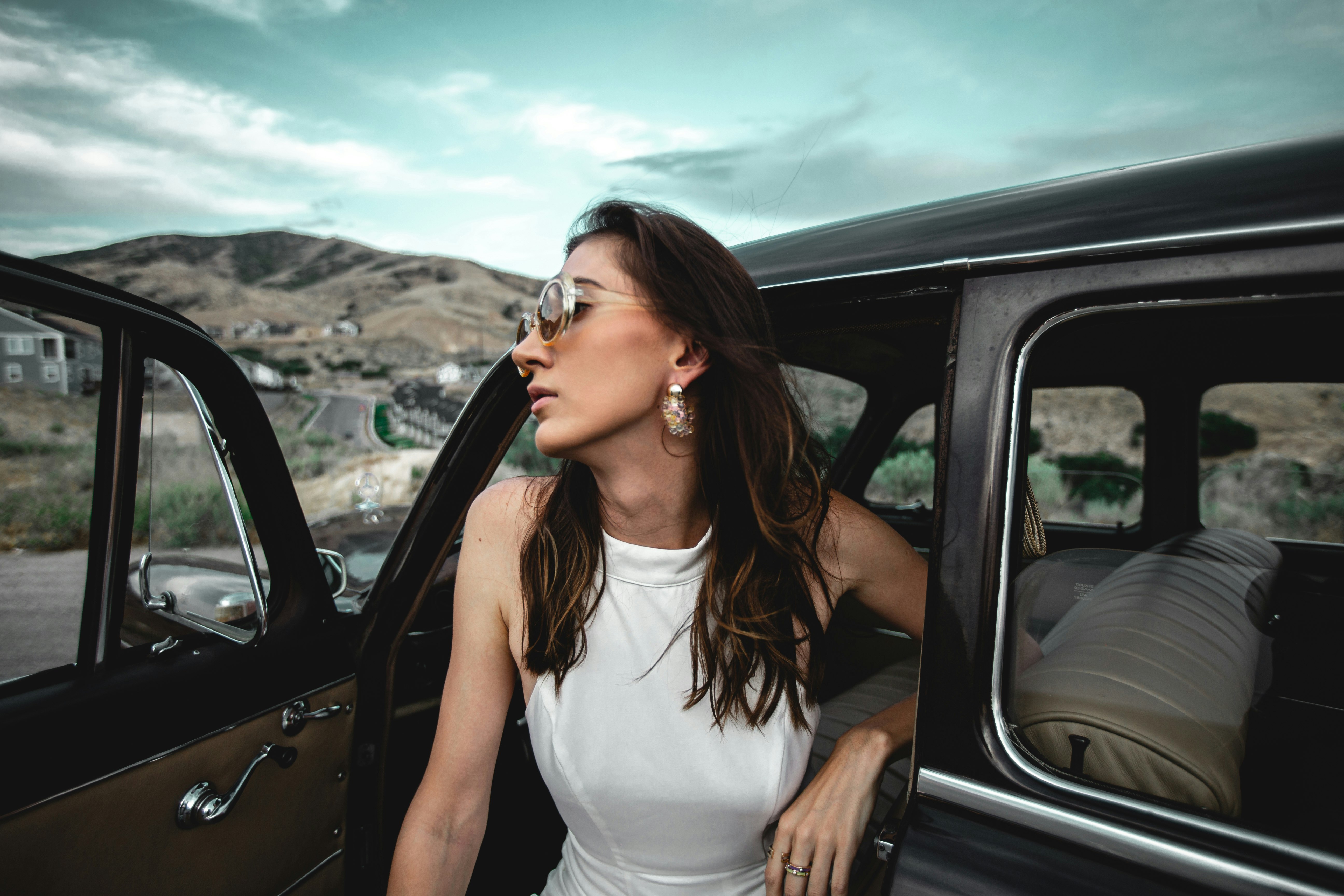 woman in white tank top standing in front of black car